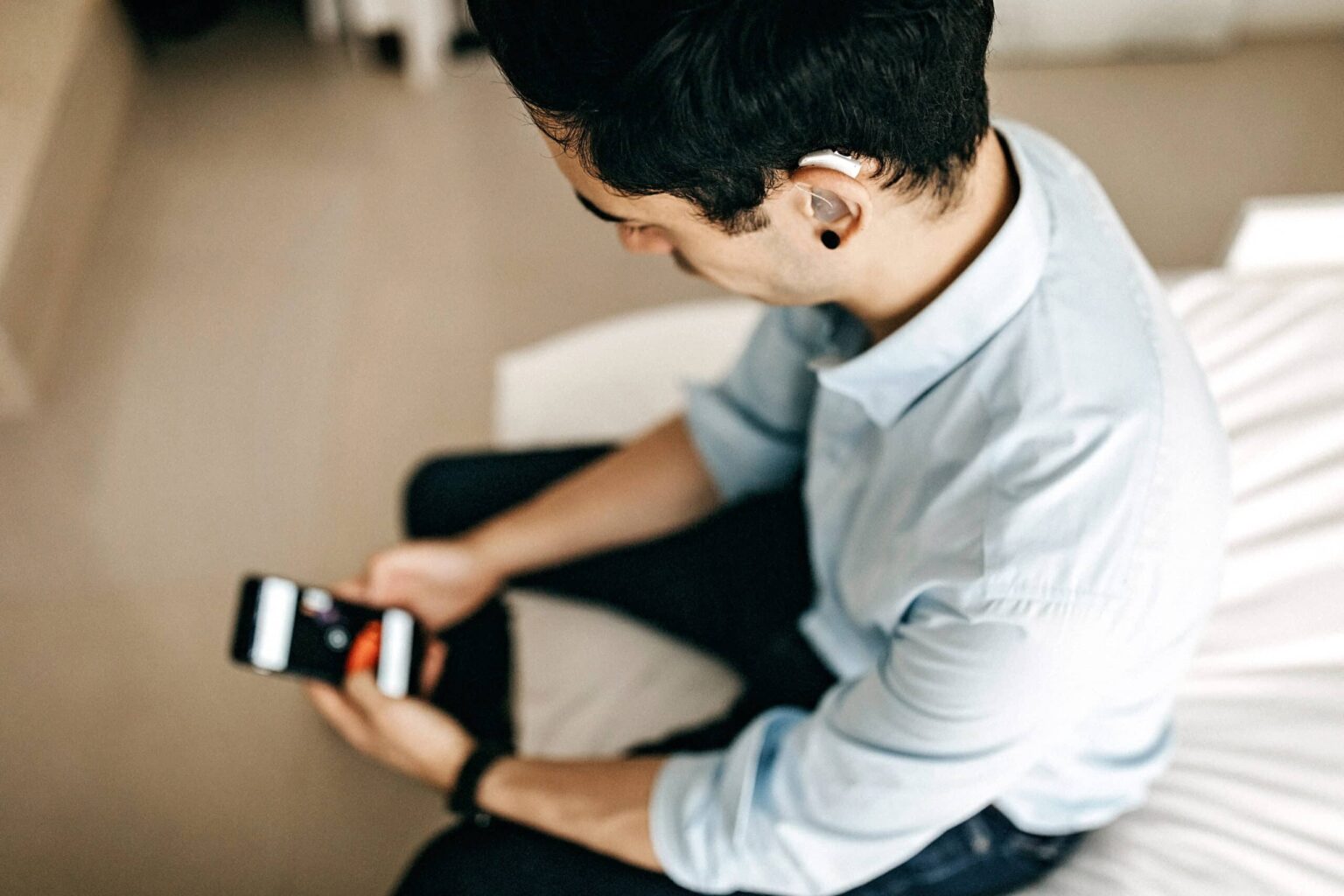 Younger businessman with a hearing aid looks at his smartphone.