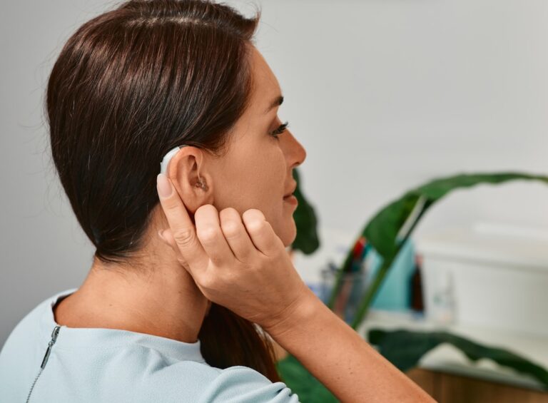 Adult woman with hearing aid behind the ear can hear sounds. Hearing loss treatment concept and hearing solutions for people with deafness Woman touching the back of her hearing aid