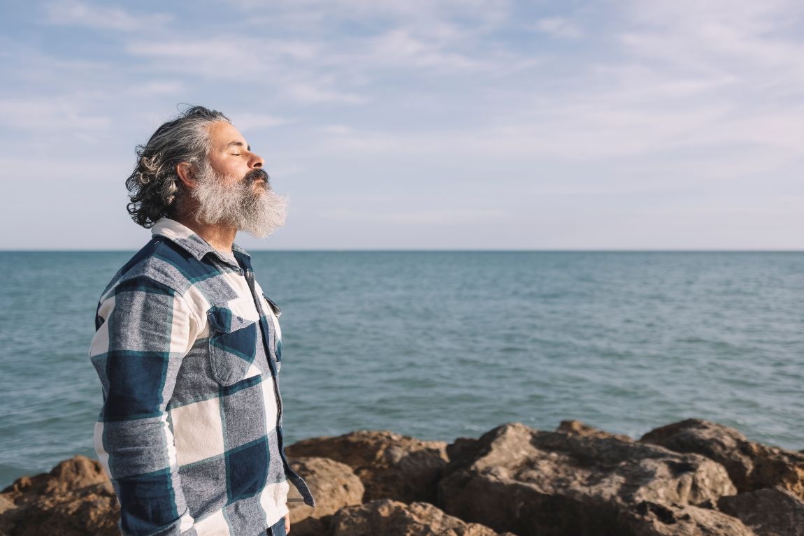 man breathing through nose on rocks near the ocean
