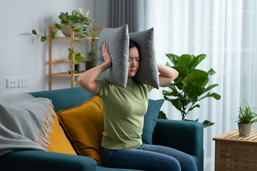 Distressed woman with sound sensitivity covers her ears with pillows to block out the sound