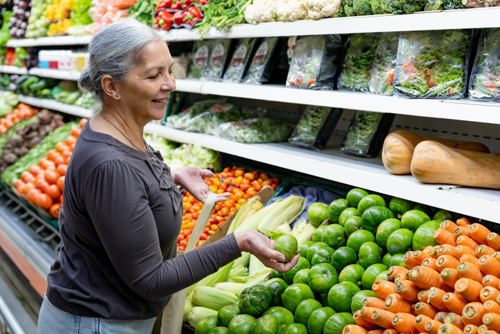 Cheerful senior woman at the supermarket choosing vegetables while holding a reusable bag